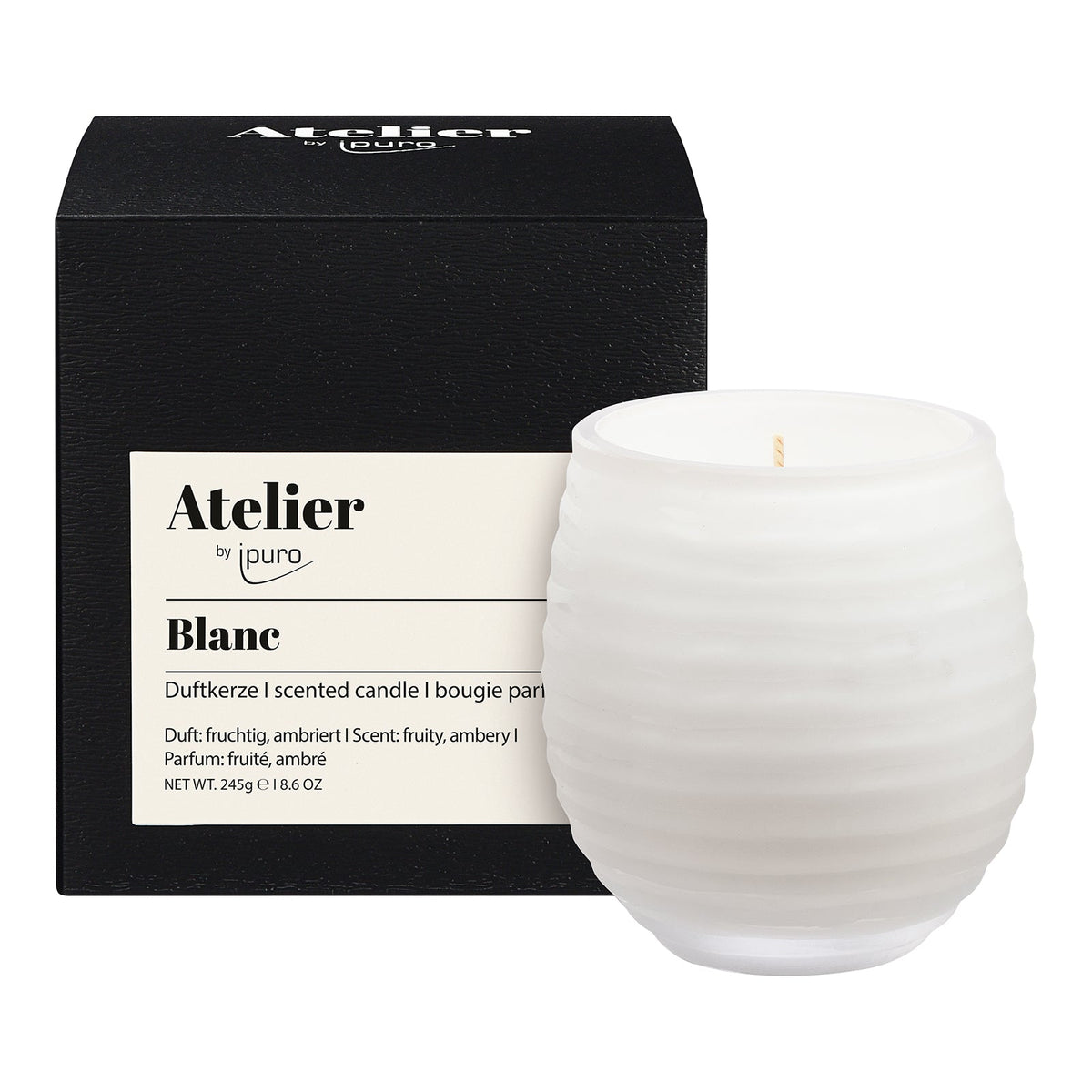 Die Atelier by ipuro blanc Duftkerze von ipuro ist eine 245g schwere Kerze aus weißem, geriffeltem Glas mit einem fruchtigen und bernsteinfarbenen Duft, die vor ihrer schwarzen Verpackung abgebildet ist.