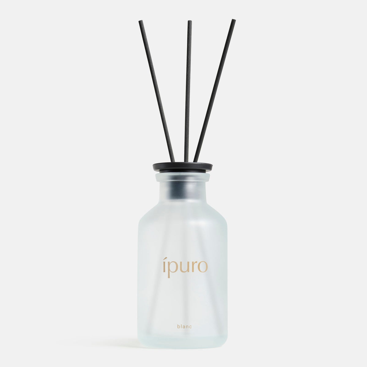 Der ipuro Raumduft CLASSIC ipuro blanc präsentiert sich in einer Milchglasflasche mit drei schwarzen Schilfrohrstäbchen, die mit Sandelholz- und Geraniennoten versetzt sind, vor einem schlichten weißen Hintergrund.