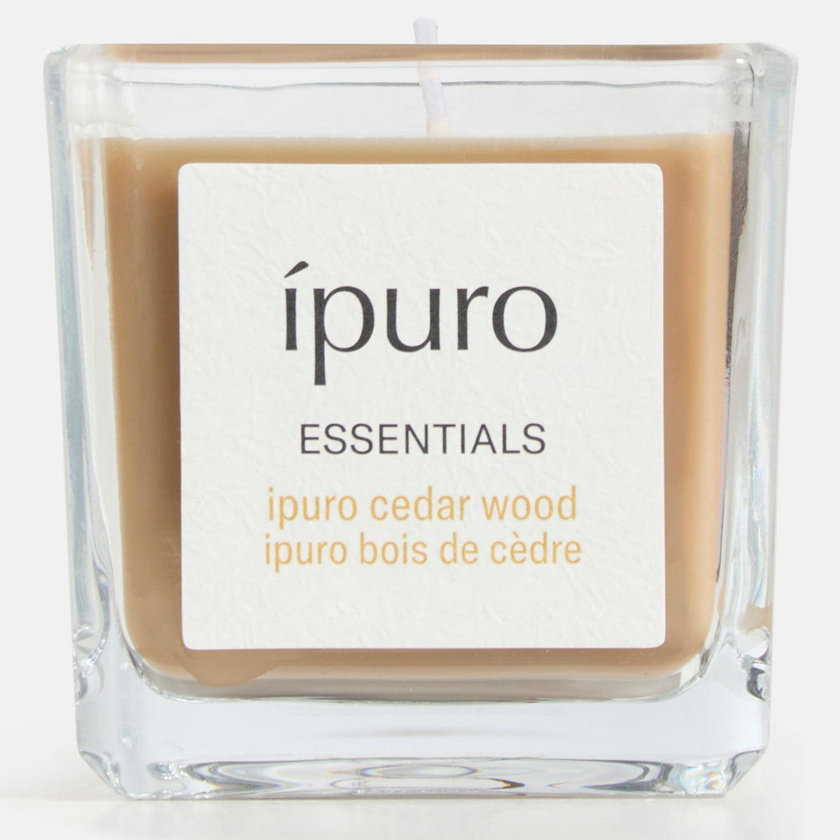 Die quadratische Glas-Duftkerze ipuro cedar wood von ipuro mit hellbraunem Wachs und einem warmen, holzigen Duft schafft eine gemütliche, einladende Atmosphäre. Die Duftangaben auf dem Etikett sind auf Englisch und Französisch.