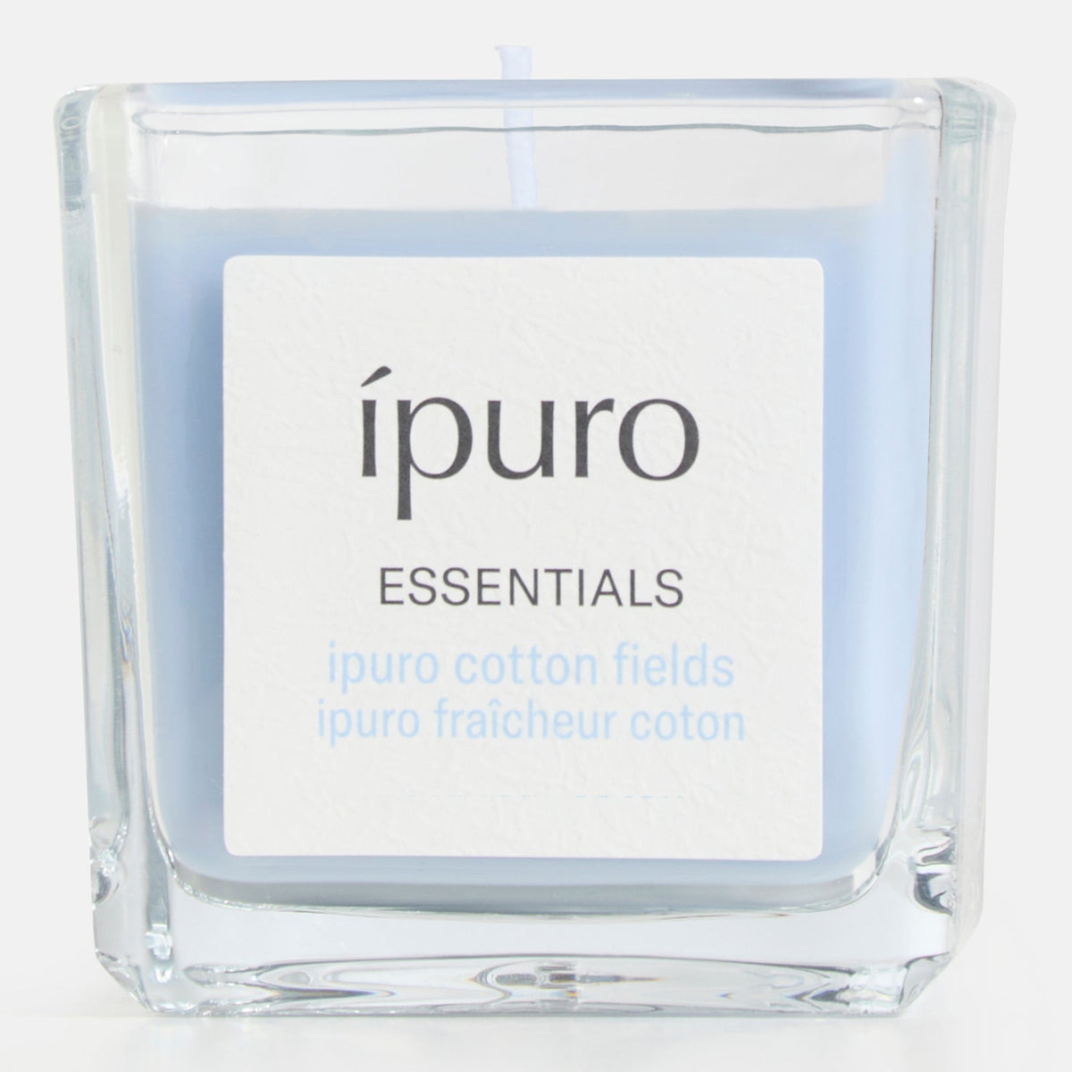 Die Duftkerze ipuro cotton fields von ipuro ist eine quadratische Glaskerze mit hellblauem Wachs und einem Etikett mit der Aufschrift "ipuro ESSENTIALS". Ihr subtiler Duft vermischt Noten von Vanille und frischer Baumwolle und verbessert Ihr Raumklima.