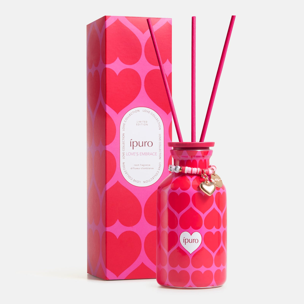 Der ipuro Raumduft love's embrace 240ml Diffusor besteht aus einem rosa und rot gemusterten Flakon mit goldenem Herzarmband, gefüllt mit Blumenduft, drei Schilfrohrstäbchen und wird in einer passenden herzverzierten Box geliefert.