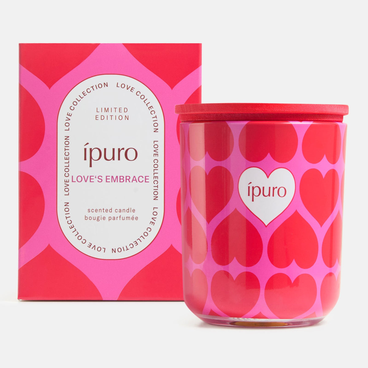 Die ipuro Kerze love's embrace 270g ist eine rosa-rote Duftkerze in einem herzförmigen Gefäß mit Sandelholz-Noten, die vor einer Schachtel mit passendem Herzmotiv steht und als limitierte Auflage von ipuro gekennzeichnet ist.