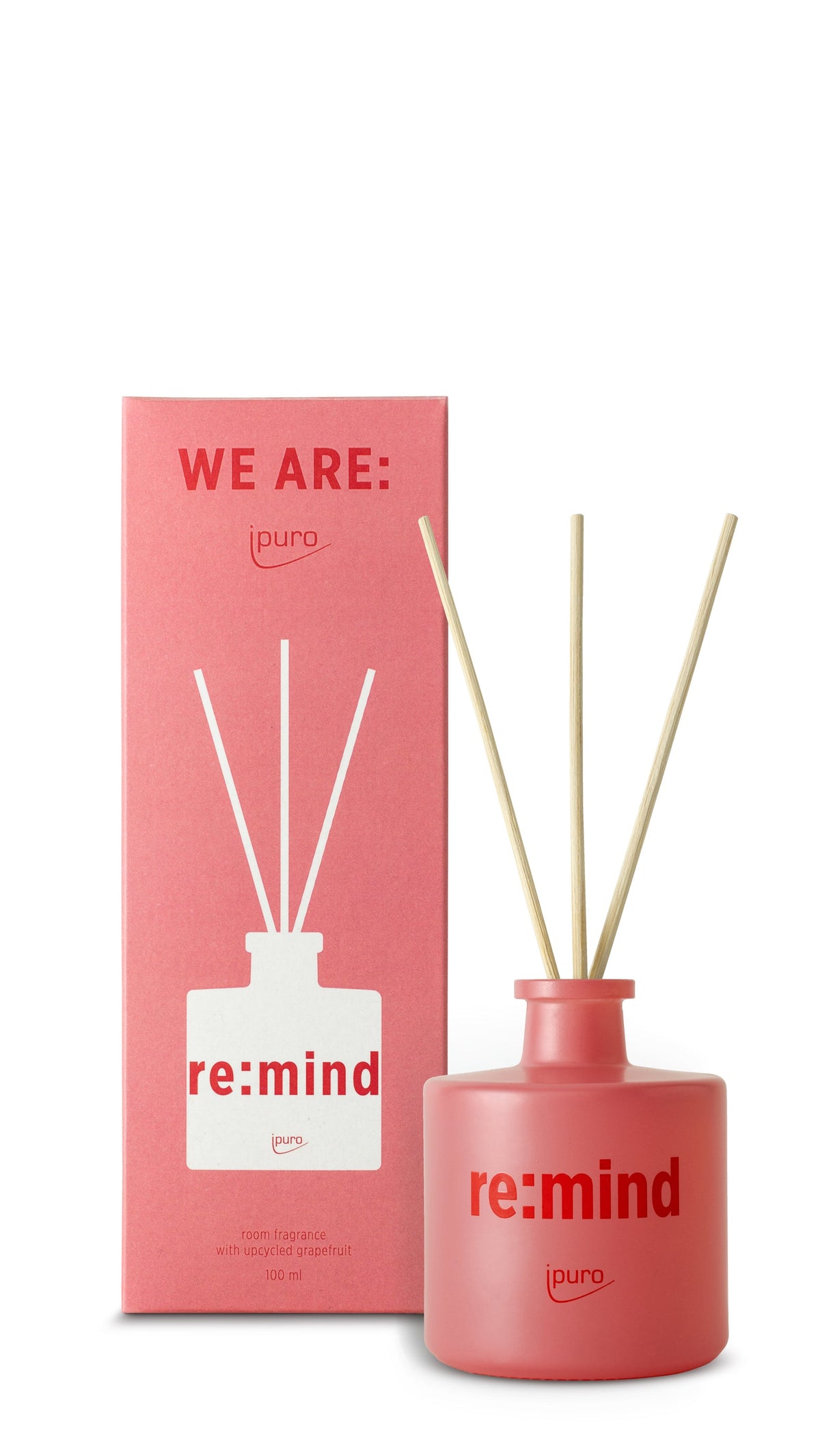 Eine rosafarbene Schachtel mit der Aufschrift "WE ARE: ipuro re:mind Raumduft" von ipuro steht neben einer passenden rosafarbenen Diffusorflasche mit der Aufschrift "re:mind", die mit drei Holzschilfrohren versehen ist und einen erfrischenden Grapefruitduft verströmt.