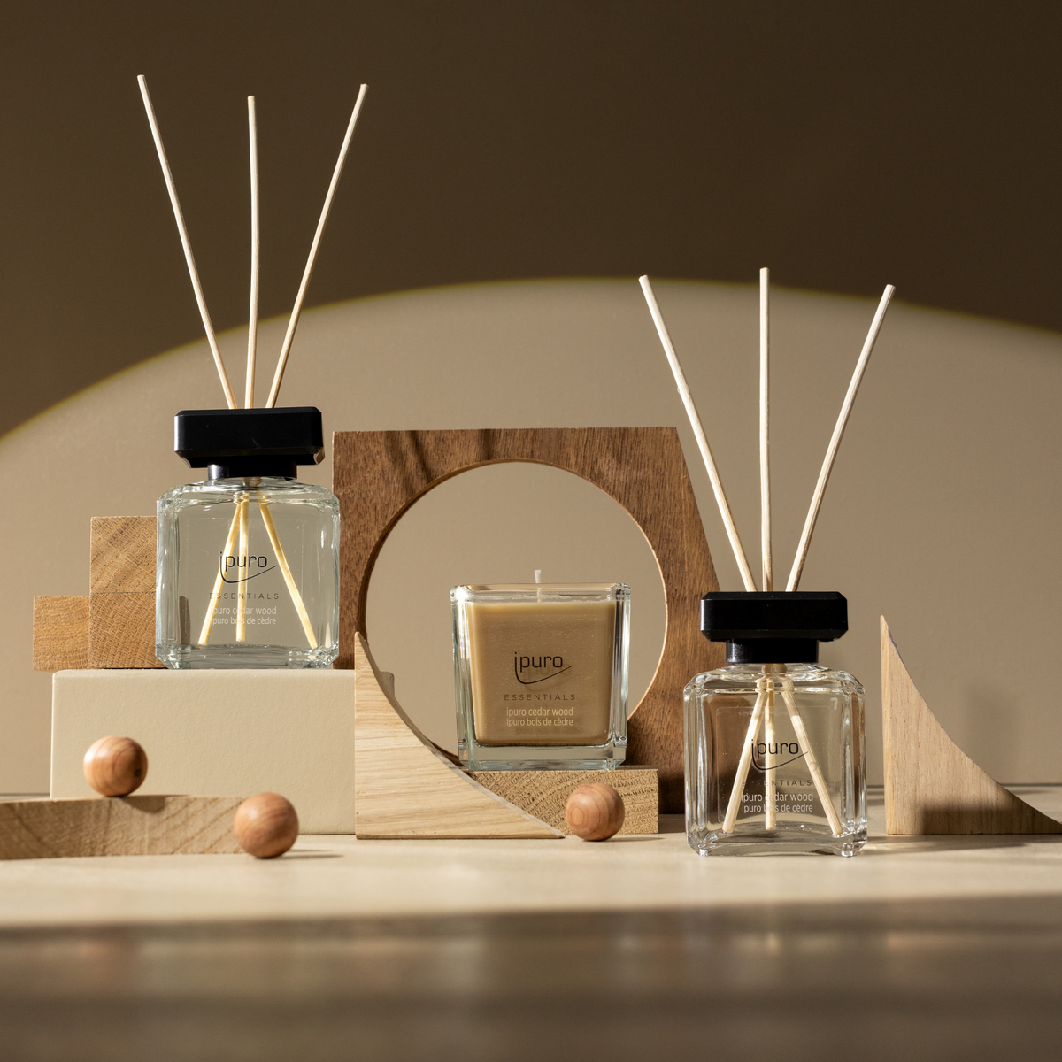 Der ESSENTIALS ipuro Zedernholz Scent Plug Refill von ipuro steht zwischen geometrischen Holzformen auf einer beigen Fläche mit warmer Beleuchtung und erfüllt die Szene mit einem gemütlichen, holzigen Duft von Zedernholz und Sandelholz.