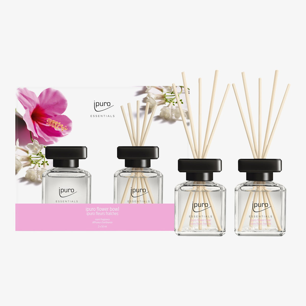 Vier gläserne ipuro ESSENTIALS Blütendiffusoren mit schwarzen Kappen und hellen Holzblättern werden vor einer floralen Verpackung präsentiert. Das Raumduft-Set ipuro flower bowl von ipuro erfüllt Ihren Raum mit einem frischen, bouquetartigen Duft.