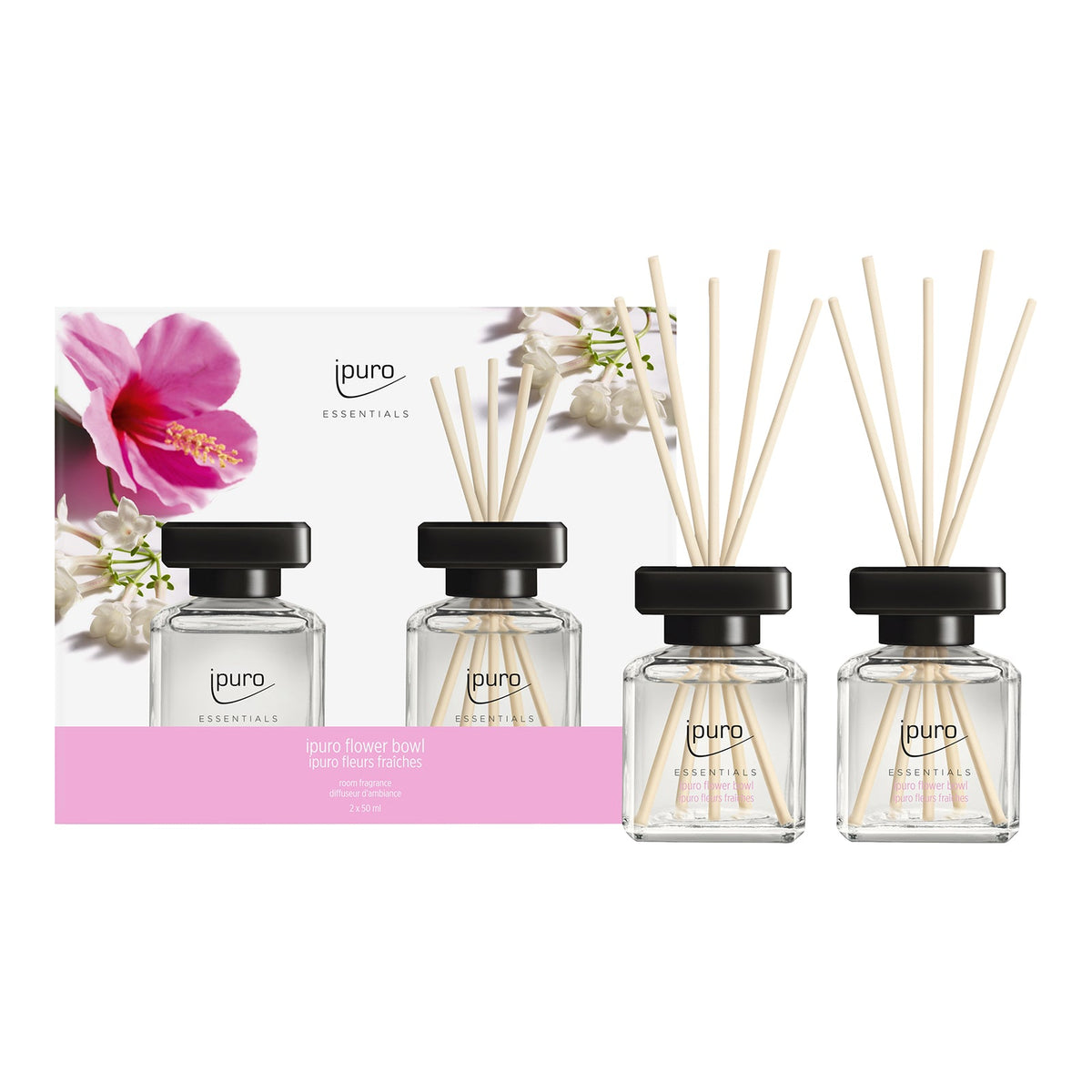 Drei gläserne Diffusorflaschen mit hölzernen Schilfrohren und schwarzen Kappen sind vor einer blumigen ipuro Essentials-Box mit der Aufschrift "Raumduft-Set ipuro flower bowl" von ipuro arrangiert, die rosa und weiße Blumen zeigt und an den Duft frischer Blüten erinnert.