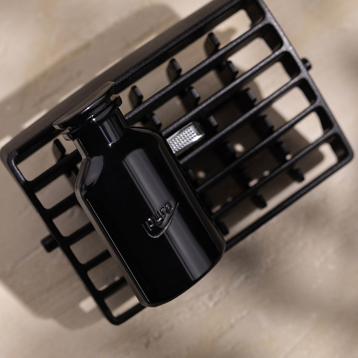 Ein glänzender schwarzer Flakon mit der Aufschrift CLASSIC ipuro noir Autoduft-Set von ipuro steht auf einem schwarzen Metallgitter auf einer beigen Oberfläche und verströmt luxuriöse Noten von Patchouli und Sandelholz.