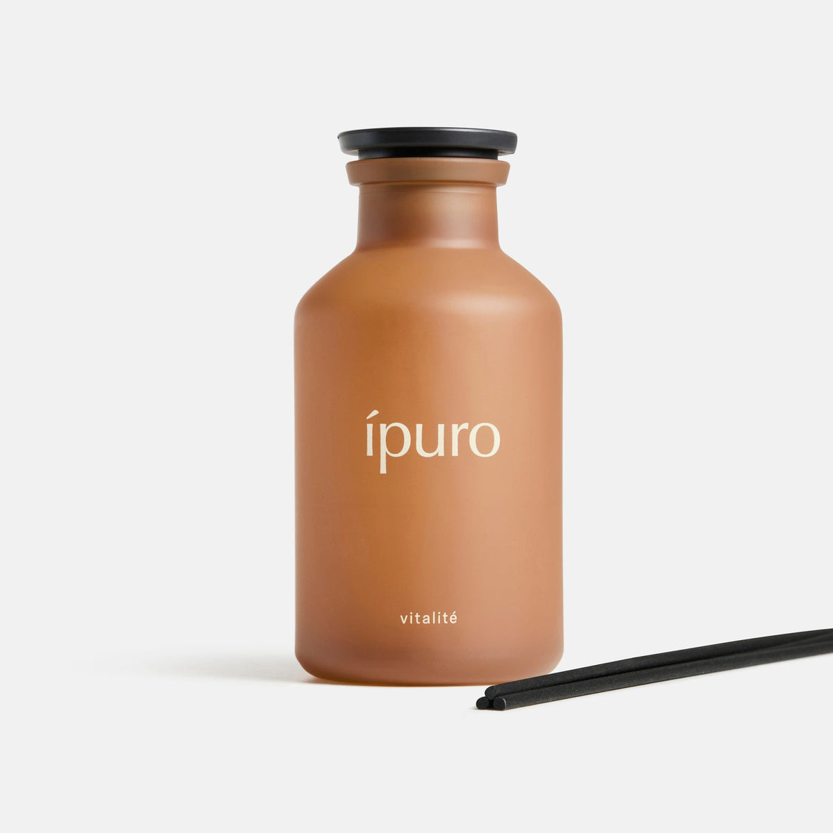 Ein mattbrauner Flakon mit der Aufschrift "Raumduft ipuro vitalité" von ipuro steht aufrecht mit einer schwarzen Kappe und zwei schwarzen Diffusorstäbchen auf weißem Grund und erinnert an Wellness mit subtilen Noten von Rosmarin und Ingwer.