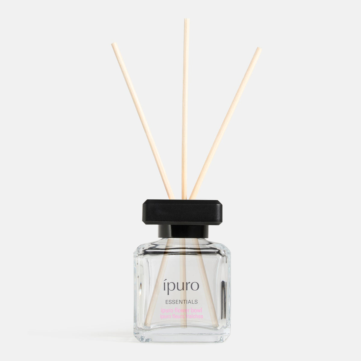Eine klare Glasflasche von ipuro Raumduft lovely flowers Diffusor mit einer schwarzen Kappe und drei hölzernen Schilfrohr, gefüllt mit duftenden Flüssigkeit von der Marke ipuro, vor einem schlichten weißen Hintergrund gesetzt.