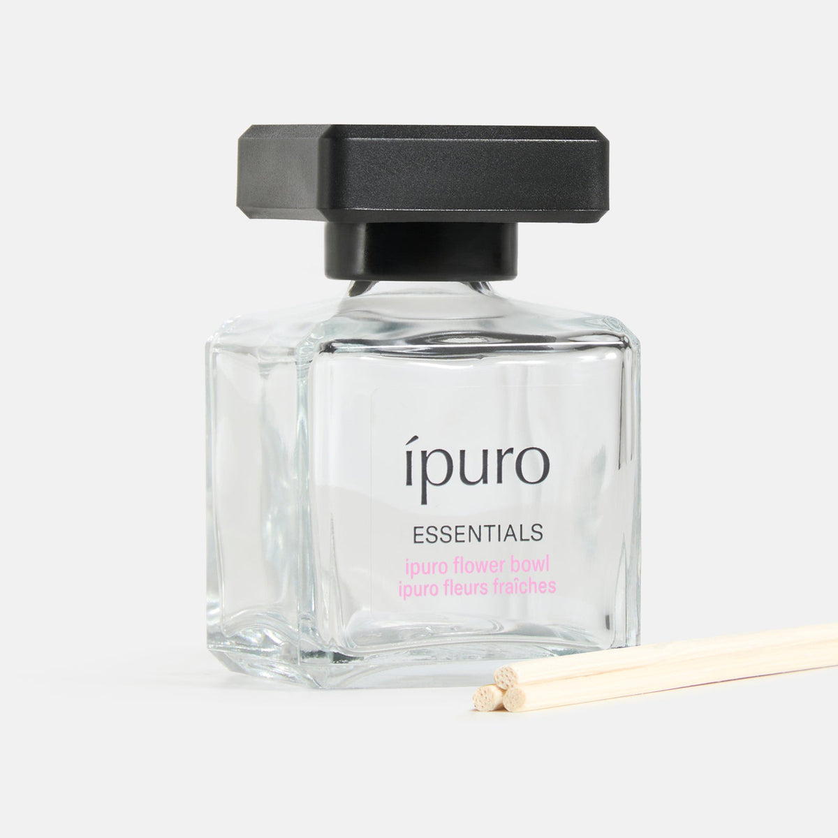 Ein klarer Glasflakon mit der Aufschrift ipuro Raumduft und einer schwarzen Kappe enthält die Duftflüssigkeit. Zwei natürliche Schilfrohrstäbchen neben dem Flakon bringen den frischen Duft von ipuro in Ihr Zuhause, vor einem beliebigen weißen Hintergrund.
