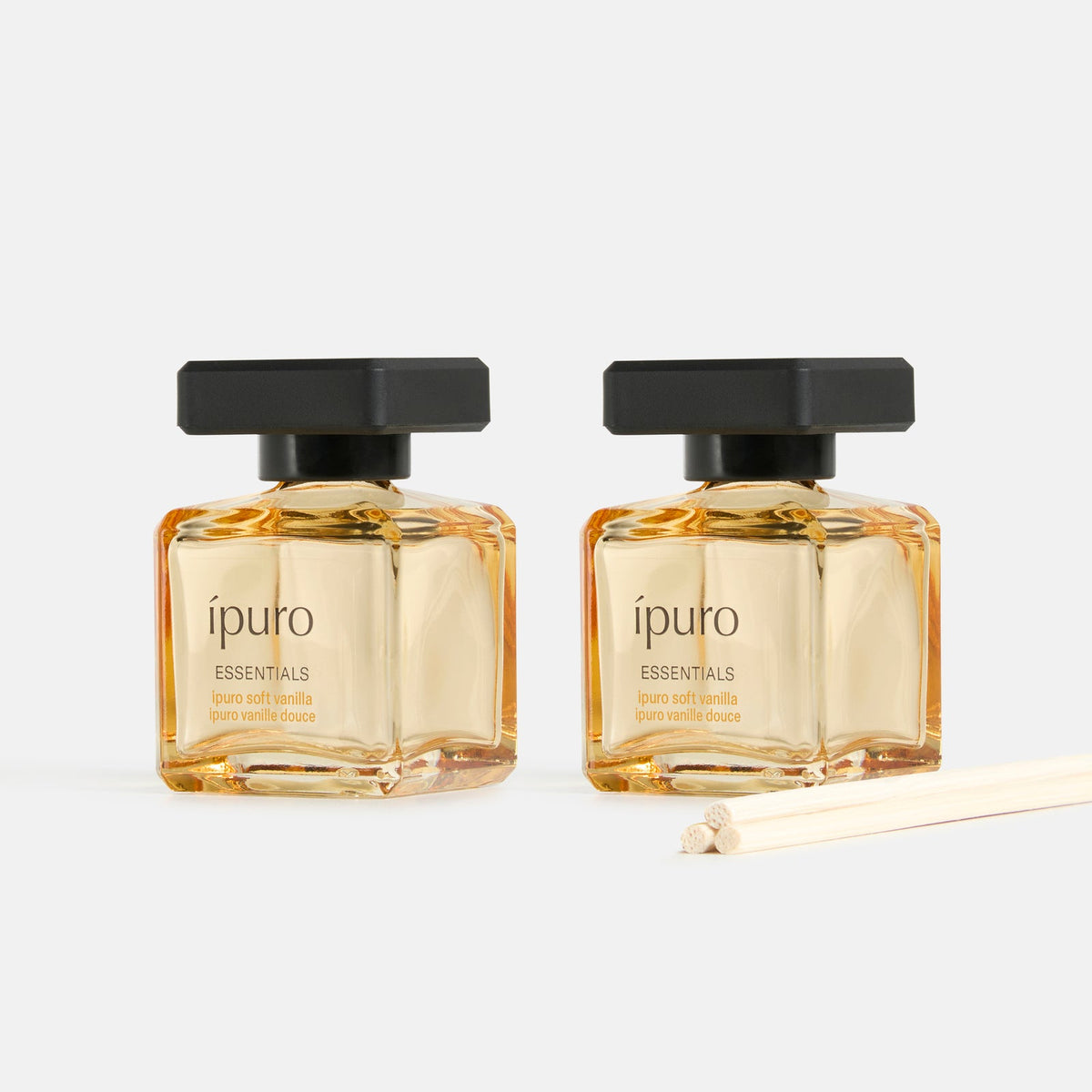Zwei quadratische Glasflakons aus dem ipuro Raumduft-Set soft vanilla mit schwarzem Verschluss und dünnen Holzstäbchen stehen nebeneinander auf hellem Grund, untermalt von Noten von Vanille und Sandelholz.