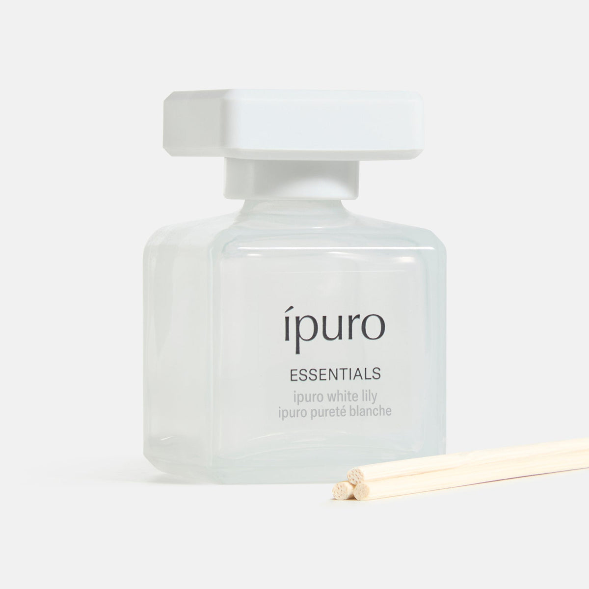 Der ipuro Raumduft white lily, eine quadratische Glasflasche mit weißem Verschluss und dünnen Holzstäbchen, bietet ein blumiges Dufterlebnis und einen zarten Duft von weißer Blüte - alles von ipuro.