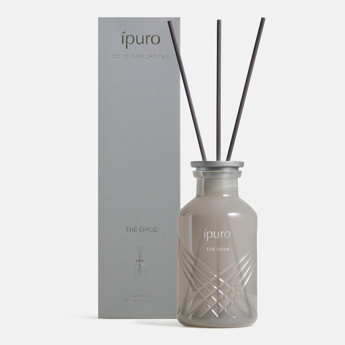 Ein Diffusor-Fläschchen aus Milchglas mit der Aufschrift ipuro Raumduft thé epicé und drei schwarzen Schilfrohren steht neben der dazu passenden hellgrauen Schachtel, beide mit dem Schriftzug "ipuro" versehen und bieten eine erfrischende Duftmischung aus Jasmin und Zitrone.